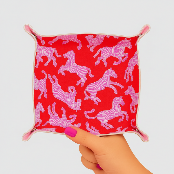 Hand holding a red square pouch with pink zebra pattern against a pink background