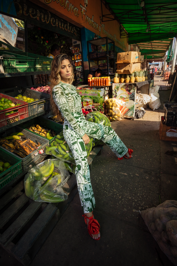 Woman in a patterned outfit sitting among produce at an outdoor market.