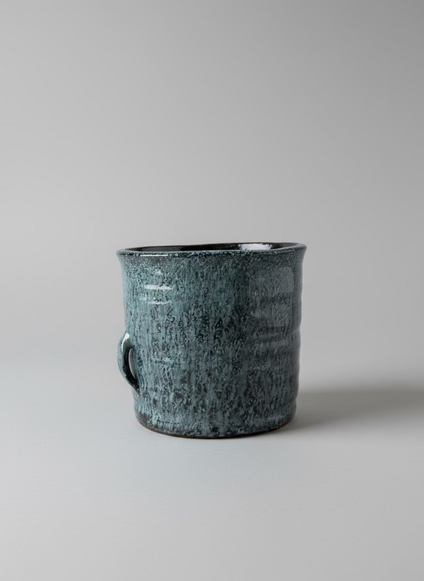 Black speckled mug on a white surface with a window in the background