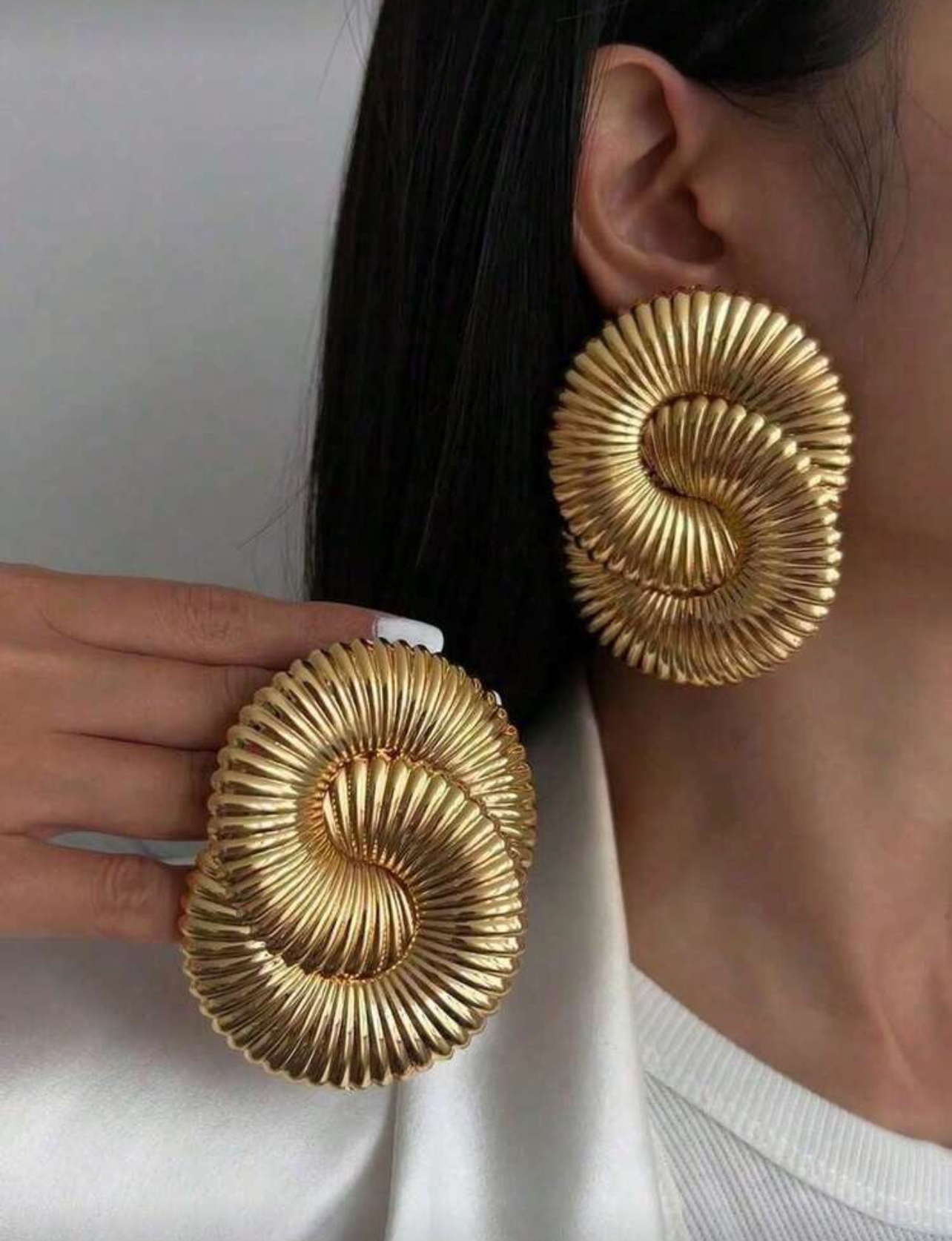 Gold spiral earrings worn by a person with a white background