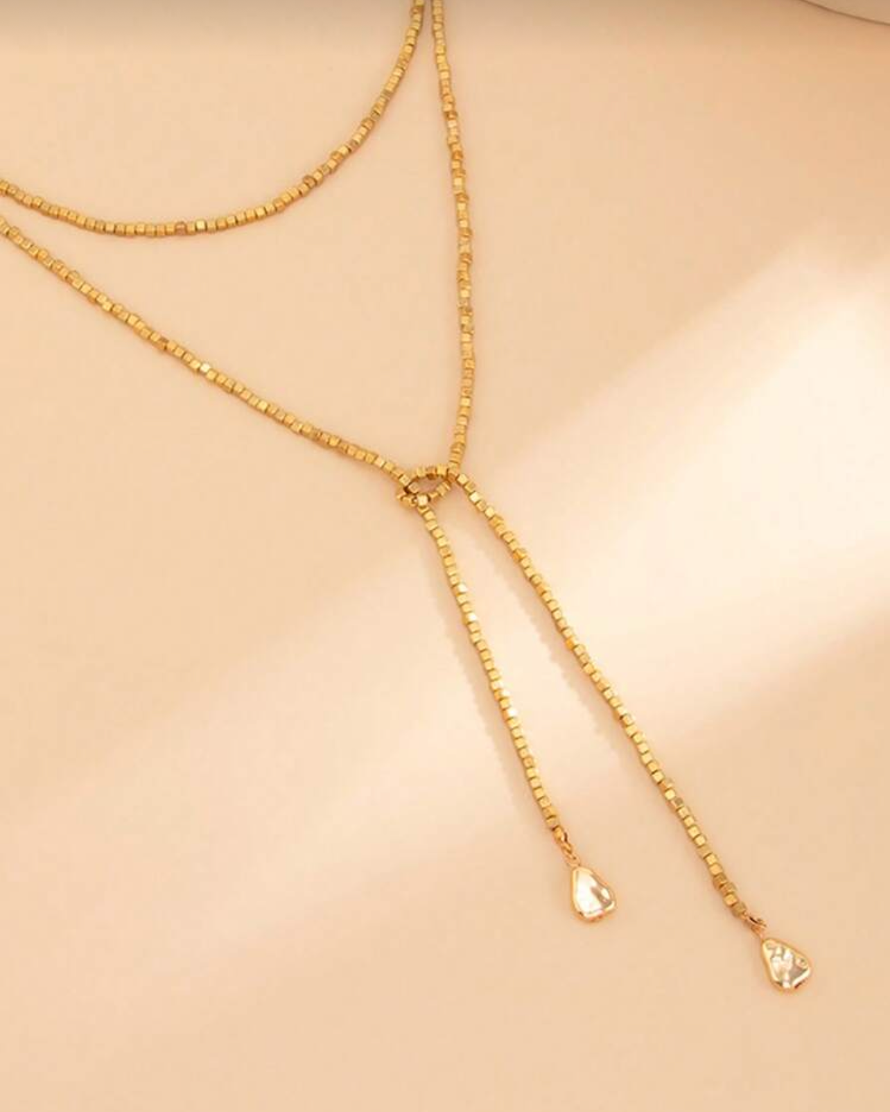 Gold necklace on a beige background with product details at the bottom.