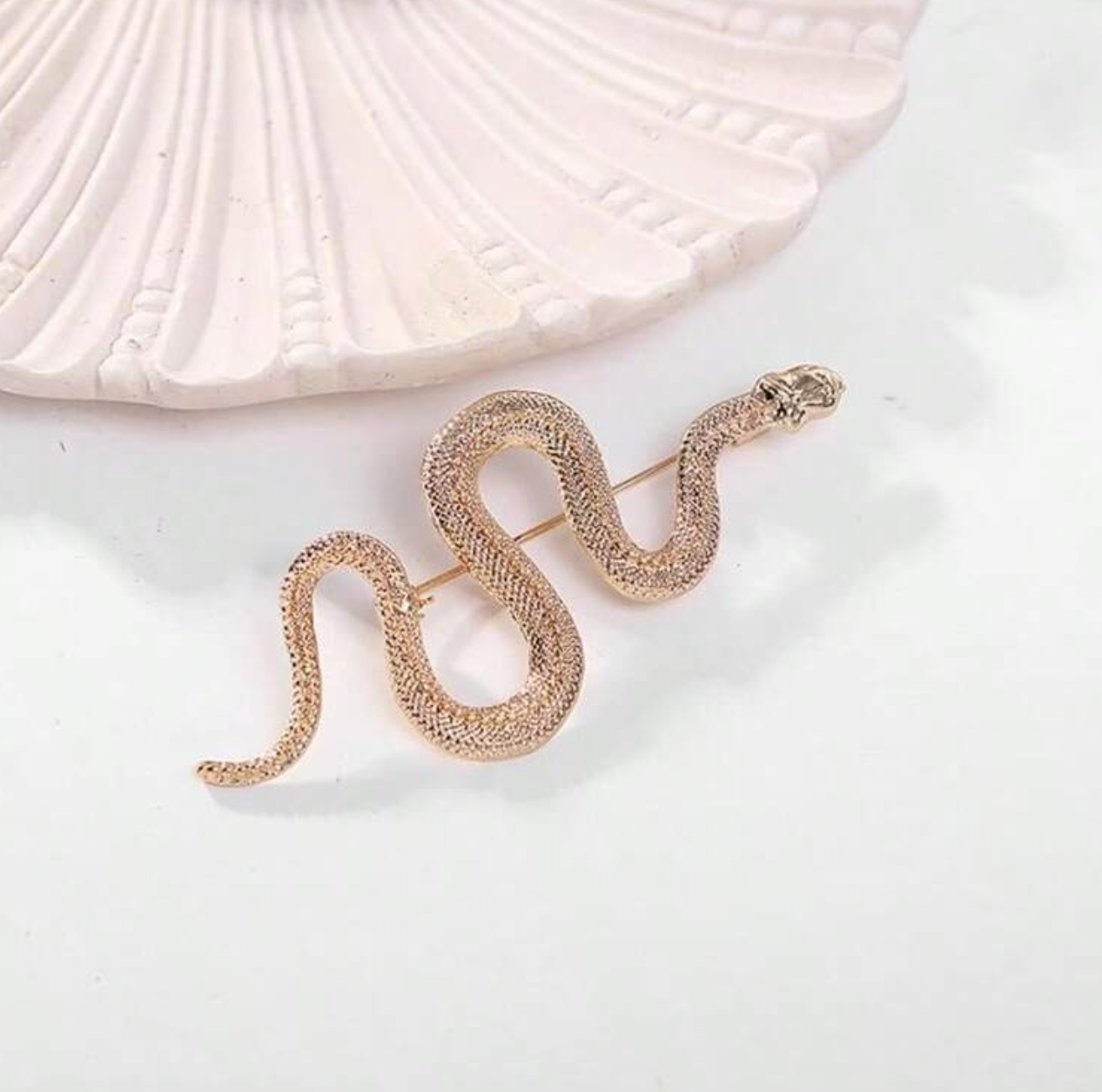Rose gold snake-shaped earrings on a white background with a shell.