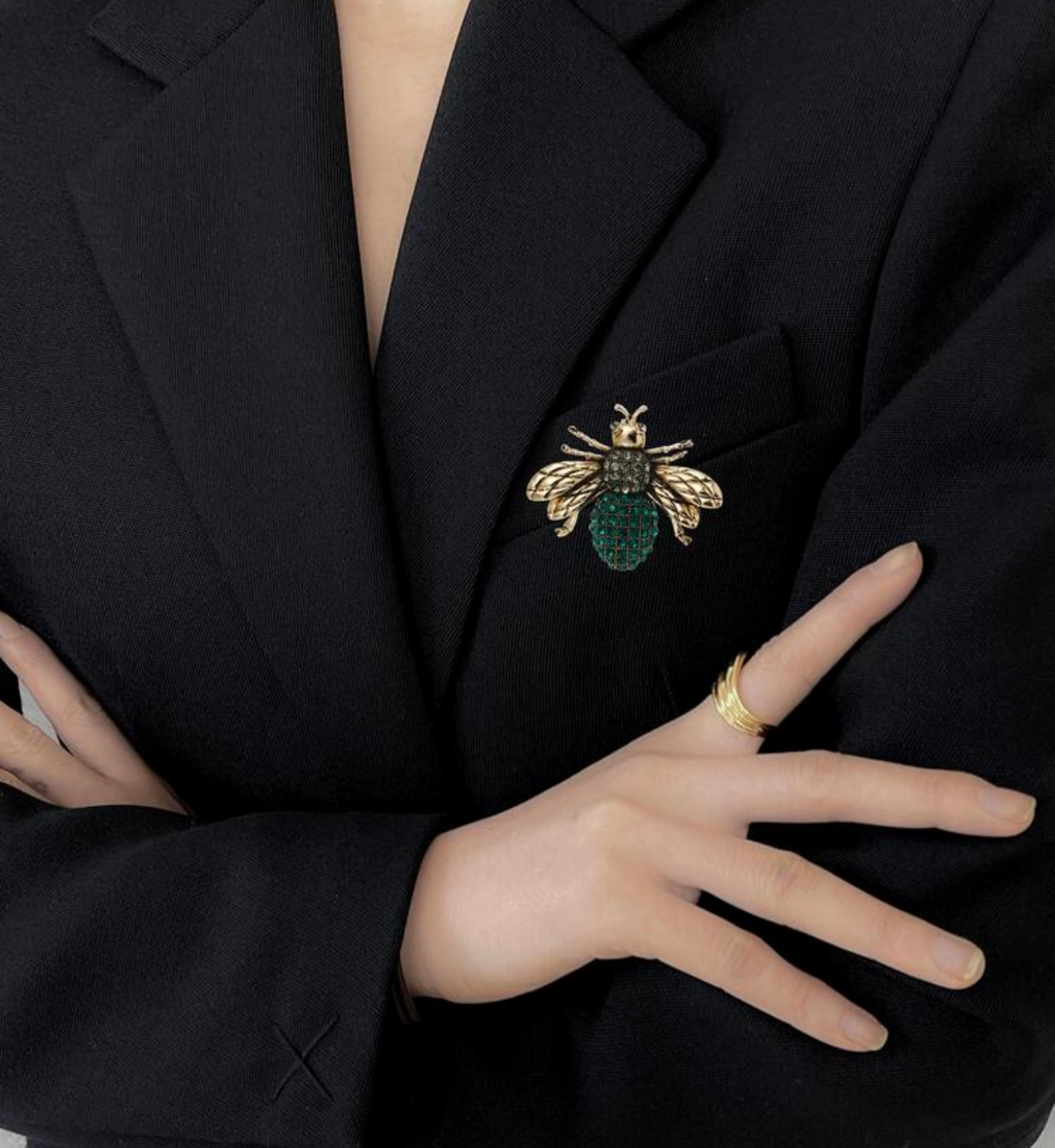 Person wearing a black blazer with a brooch, on a plain background