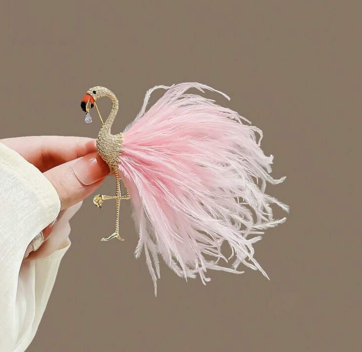 Pink feathered flamingo toy held by a hand with a dark background
